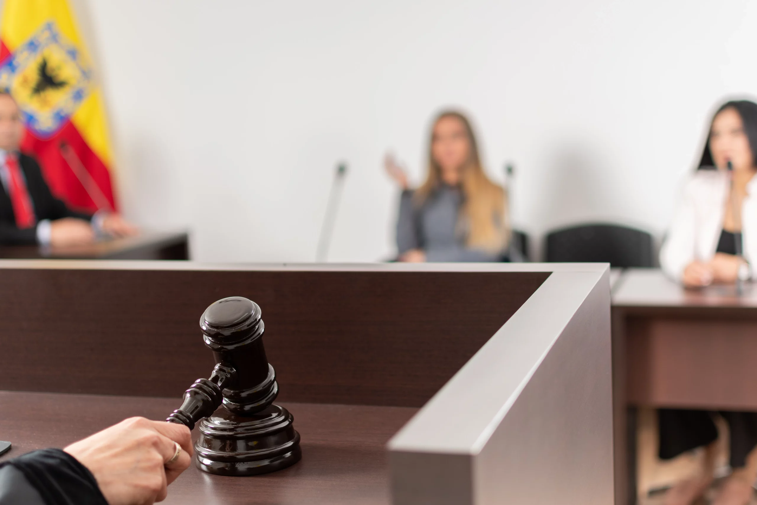 Gavel on judge's bench in courtroom during first criminal court appearance, with judge and participants blurred in background.