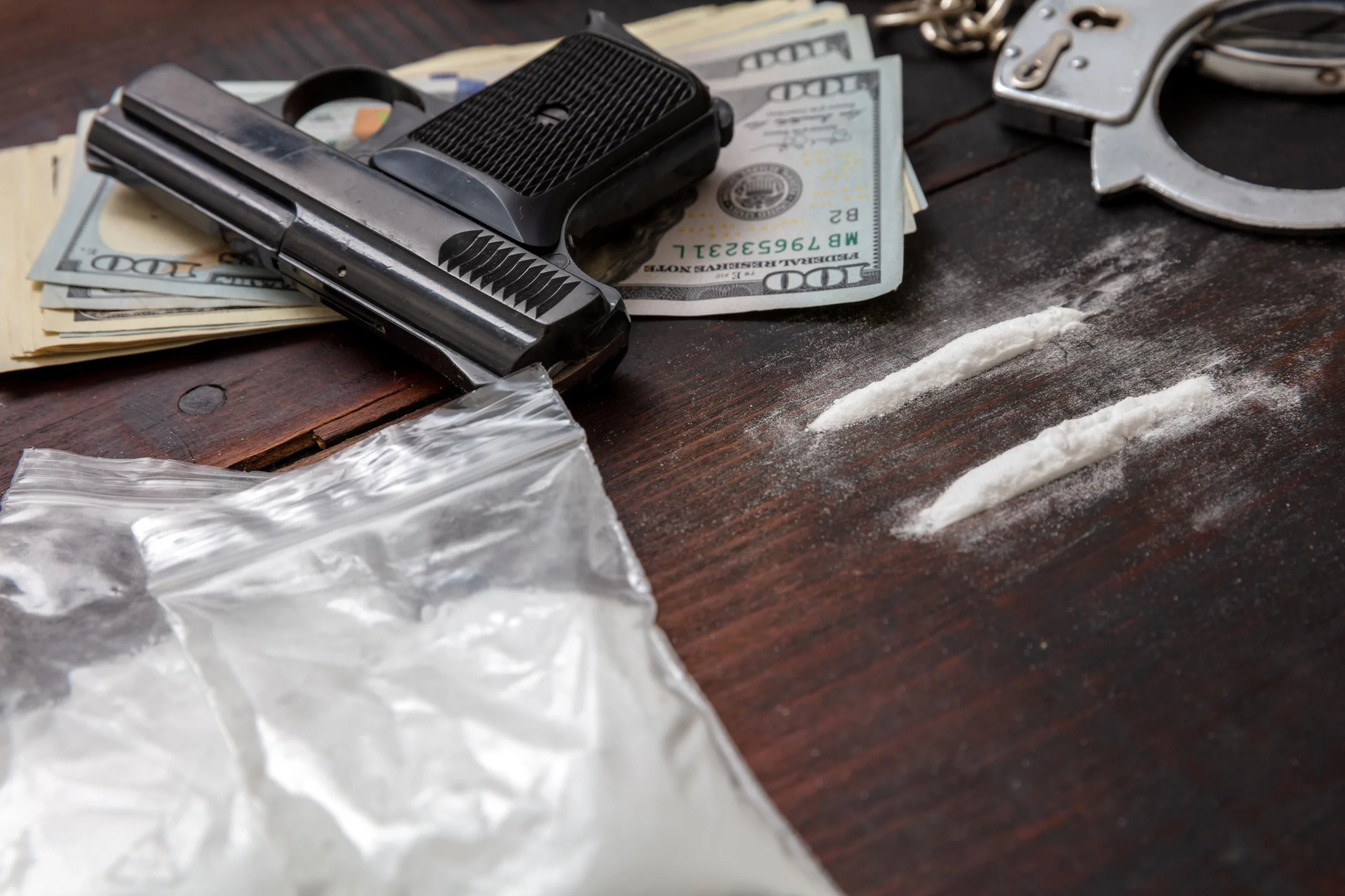 Gun, drugs, cash, and handcuffs on table symbolizing felony vs. misdemeanor drug charges in California.