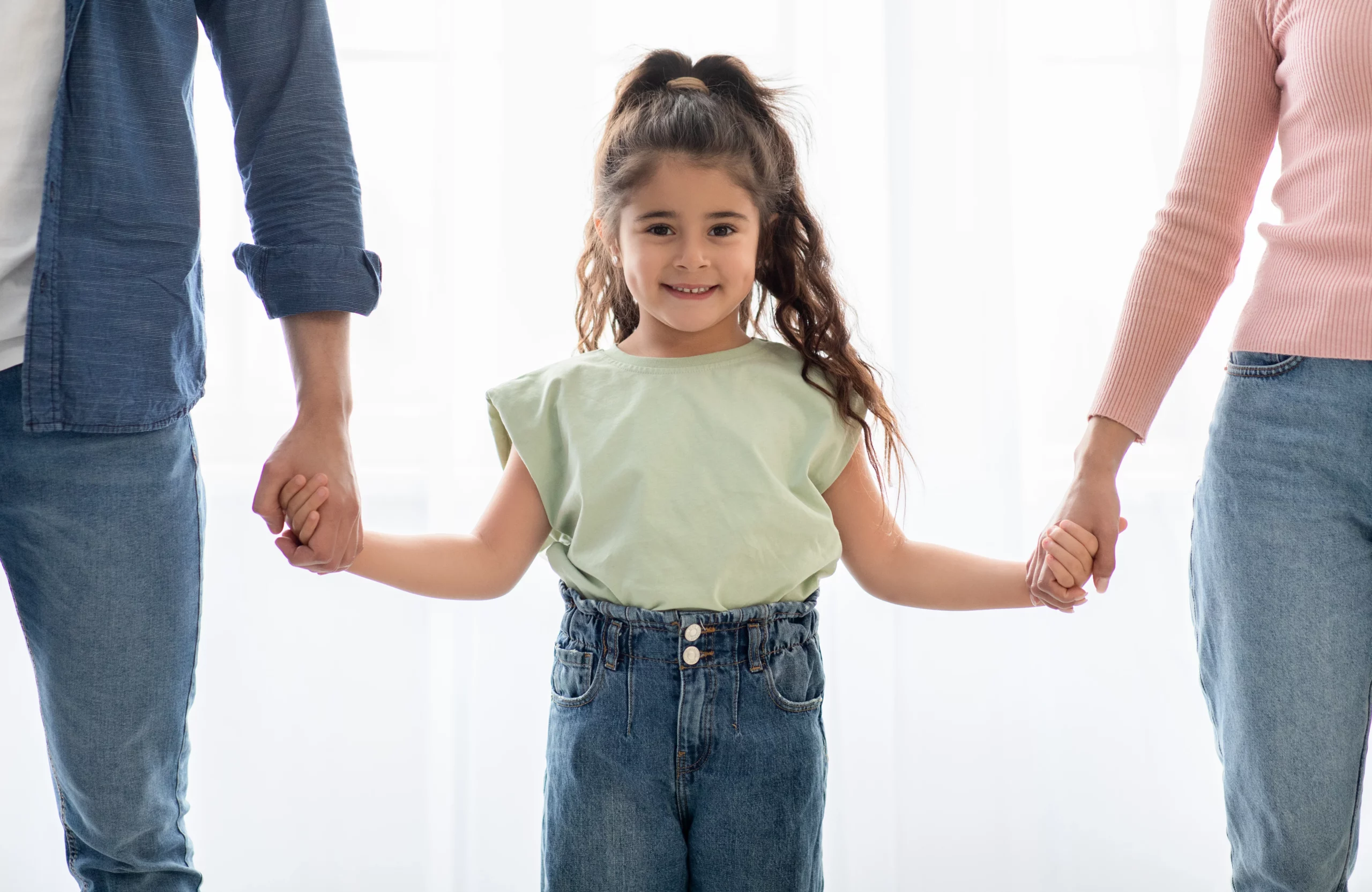 Smiling young girl holding hands with both parents, representing California child custody cases where courts prioritize the child’s best interests when determining equal or joint custody.