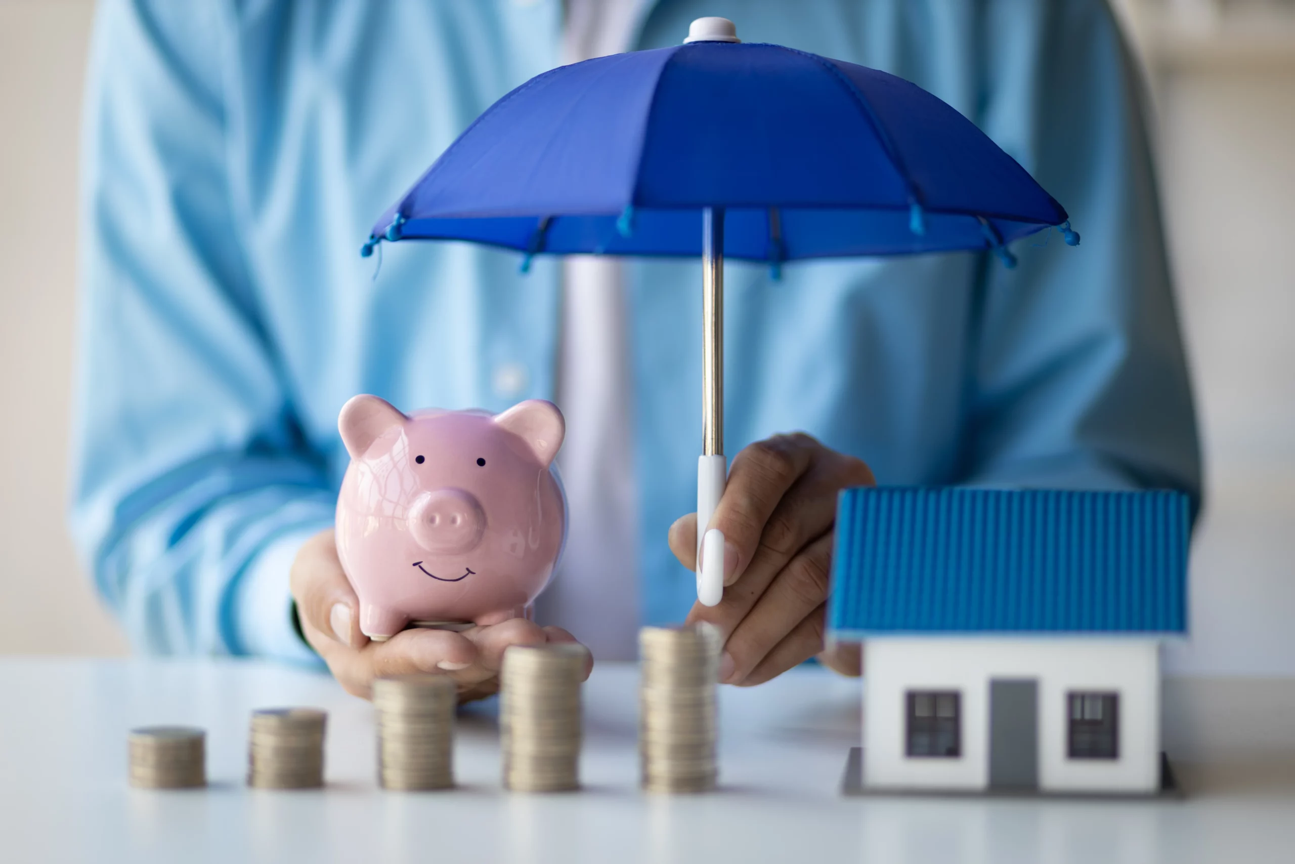 Person holding an umbrella over a house model and piggy bank, symbolizing asset protection myths and how a revocable living trust in California does not shield assets from creditor claims.