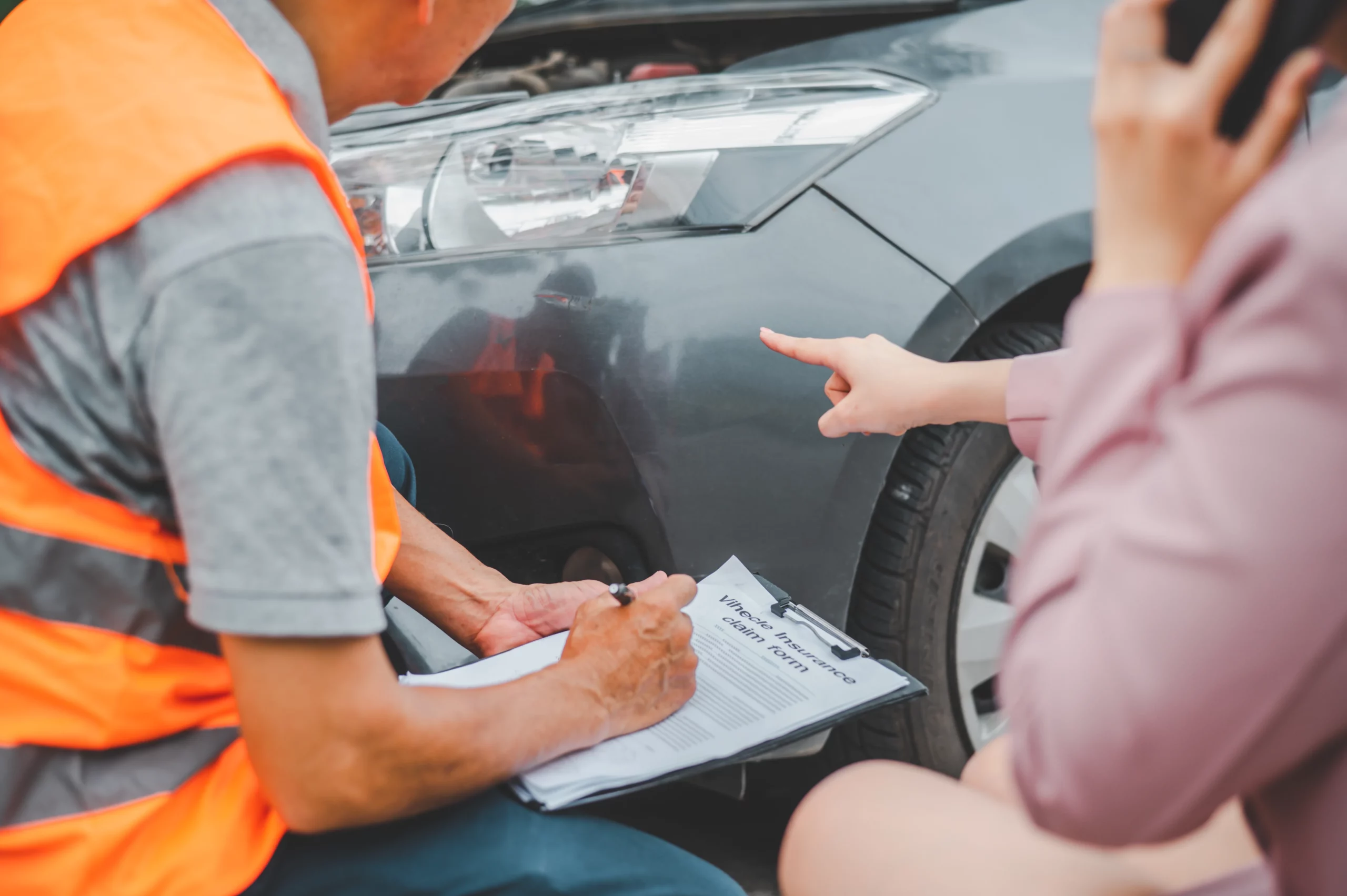 Person documenting a vehicle accident on a clipboard while inspecting car damage, representing how insurance companies may undervalue car accident claims in California and the importance of proper evidence.