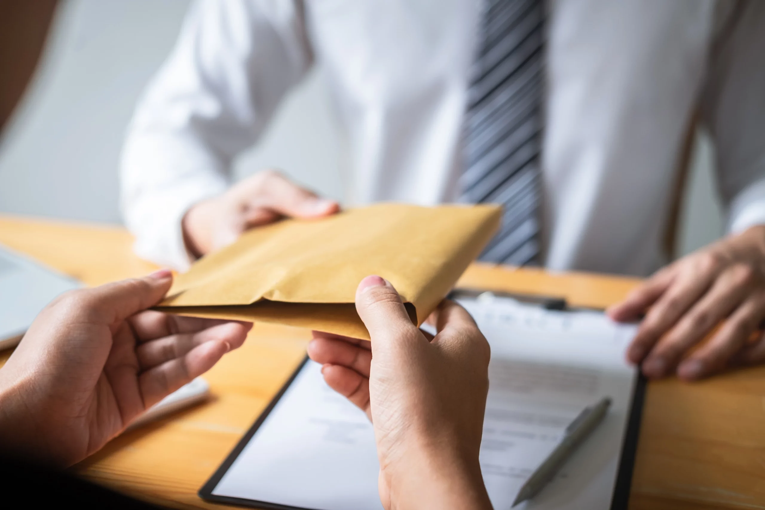 Two individuals exchanging a brown envelope over documents at a table, representing filing a government claim against a city or county in California for a personal injury case