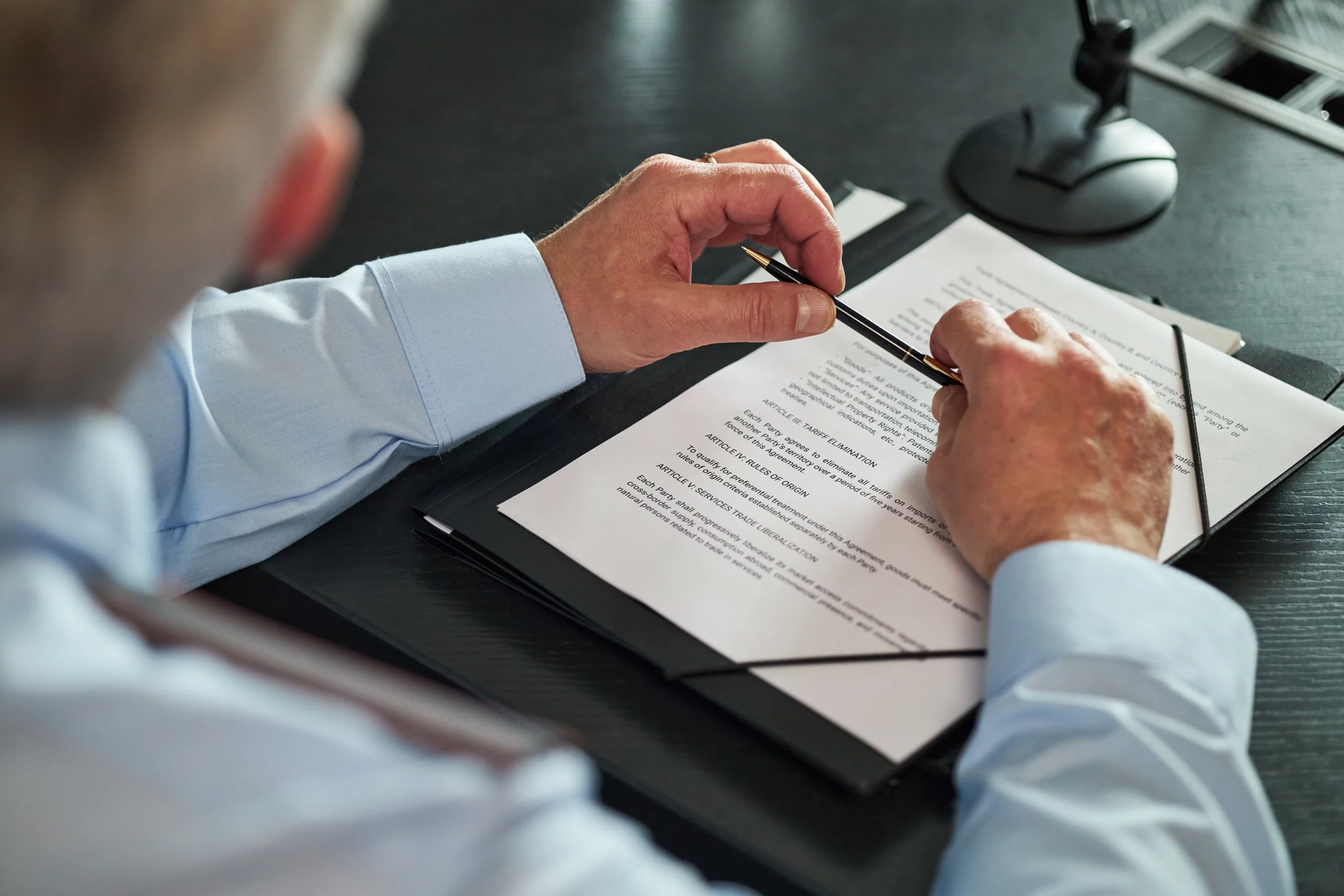 Person in a light blue shirt reviewing legal documents on a desk with a pen, representing California durable power of attorney and estate planning decision-making.